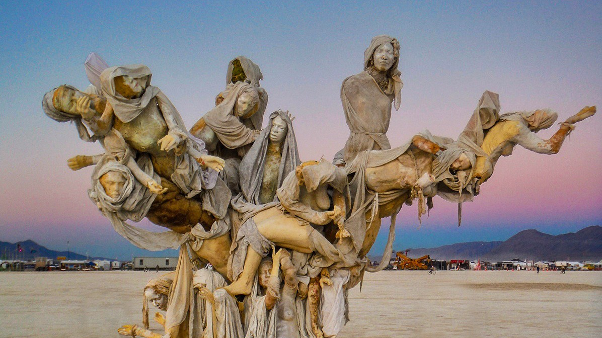 A cluster of shrouded figures suspended in flight above the Black Rock Desert playa at dusk