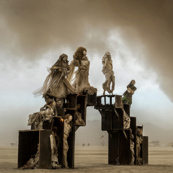 Robed figures perched atop weathered wooden crates on the playa, beneath an approaching dust storm