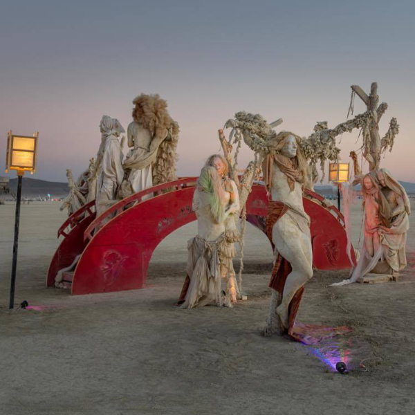 Robed figures beside a glowing red arched bridge on the playa at dusk