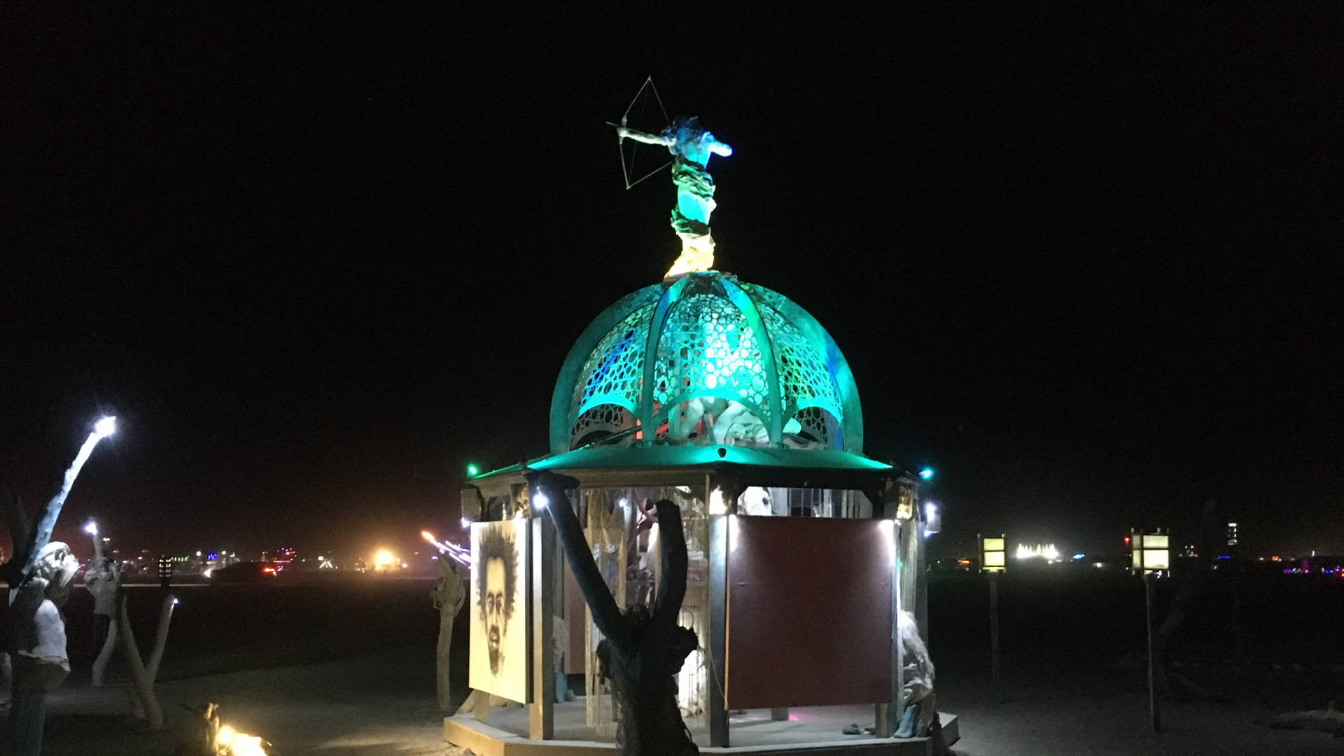 The illuminated central dome of a Valerie Mallory art installation at night, with an archer figure on top