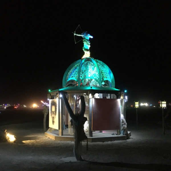 The illuminated central dome of a Valerie Mallory art installation at night, with an archer figure on top